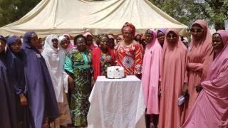 Group of people standing outside gathered around a cake on a table
