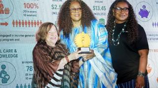 Three women at an awards ceremony holding up a gold trophy in front of a backdrop