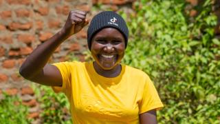 A young woman (Jennifer) pictured chest up smiling and holding her arm up in a fist