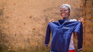 Faith proudly holding up a knitted school uniform jumper. Photo credit: Monilekan