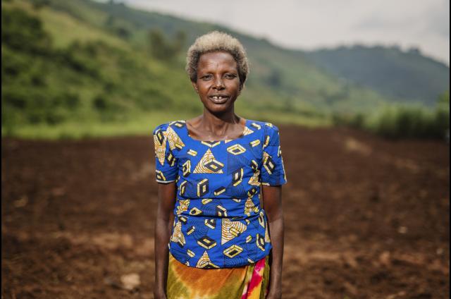 Woman survivor of war stands in a field in Rwanda.