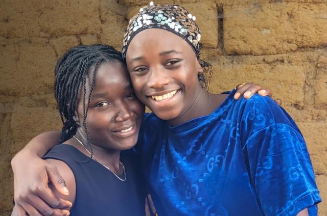 Two girls pictured chest up hugging and smiling
